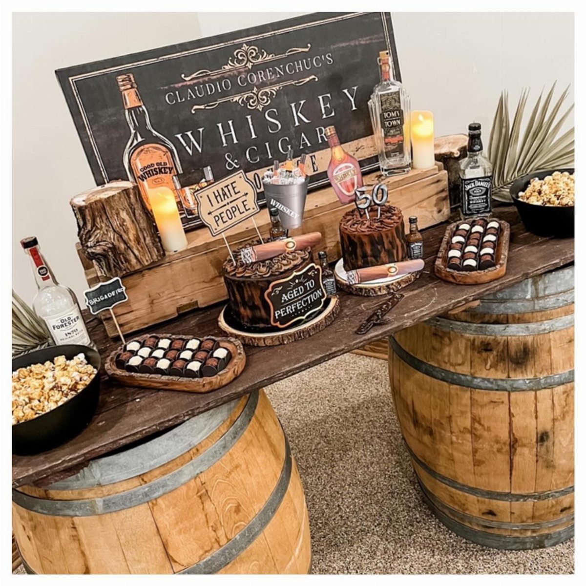 Whiskey and cigar themed party display on wooden barrels with cakes and treats.