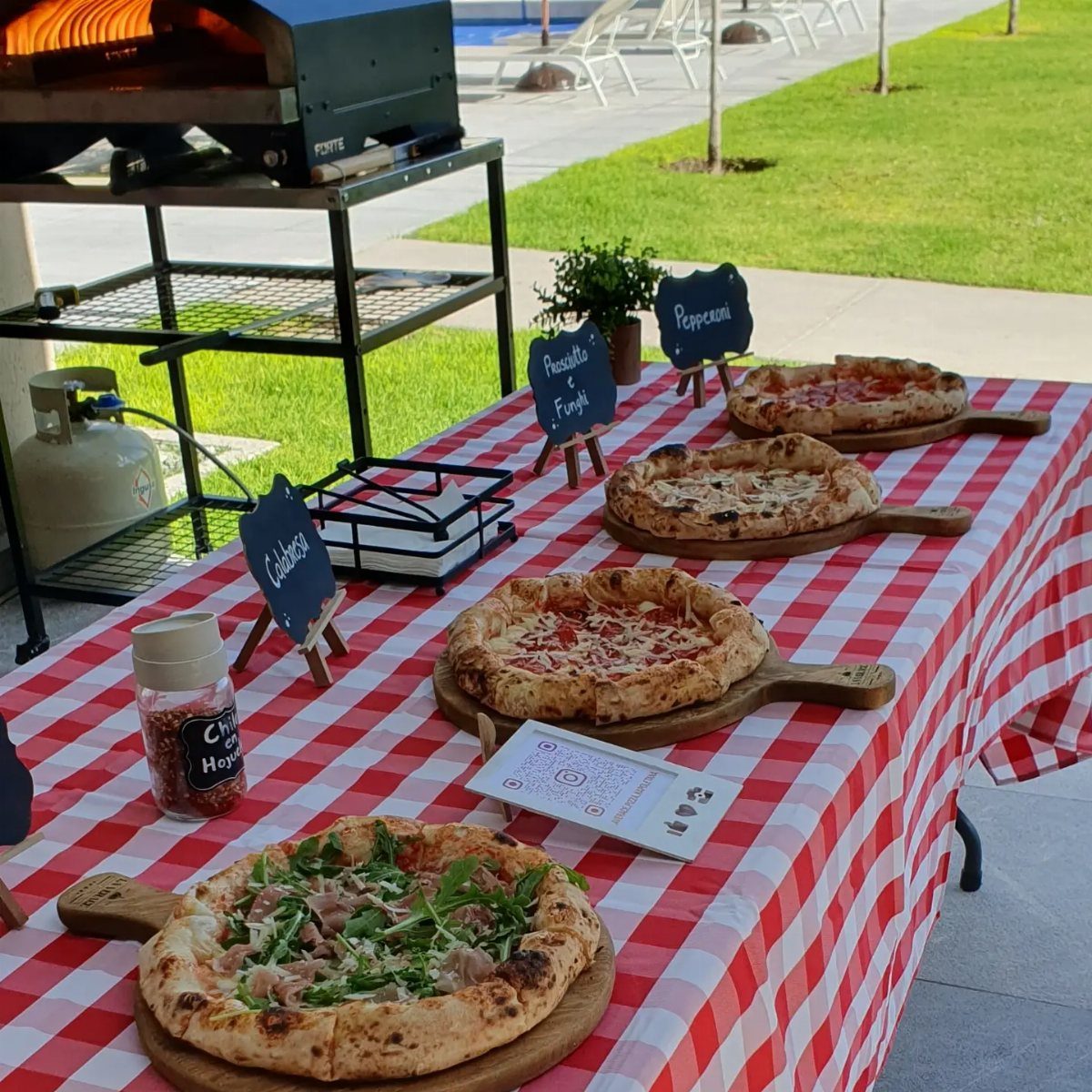 Outdoor pizza oven and four fresh pizzas on a red checkered table