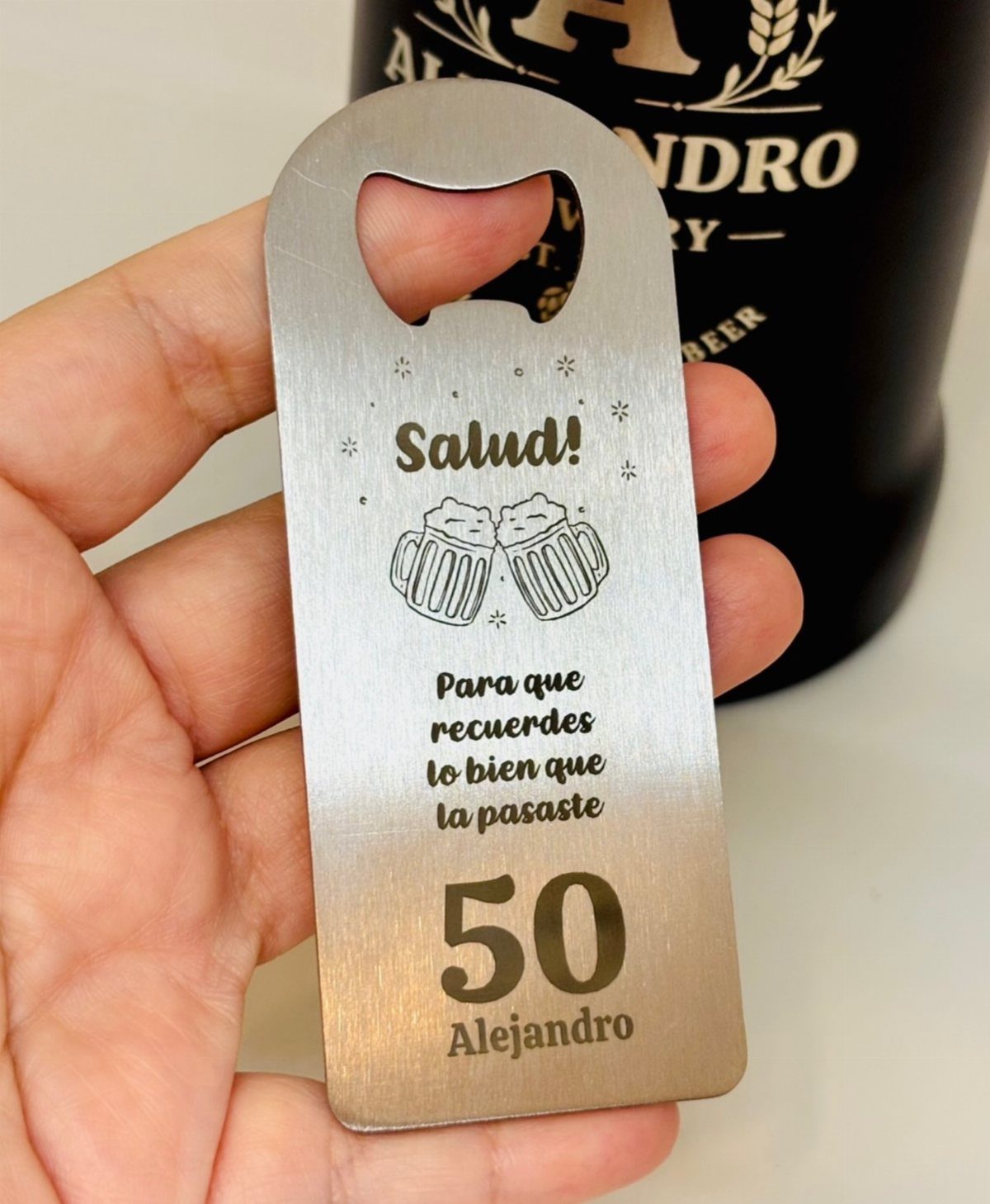 Engraved silver metal bottle opener for a 50th birthday, held in a hand.