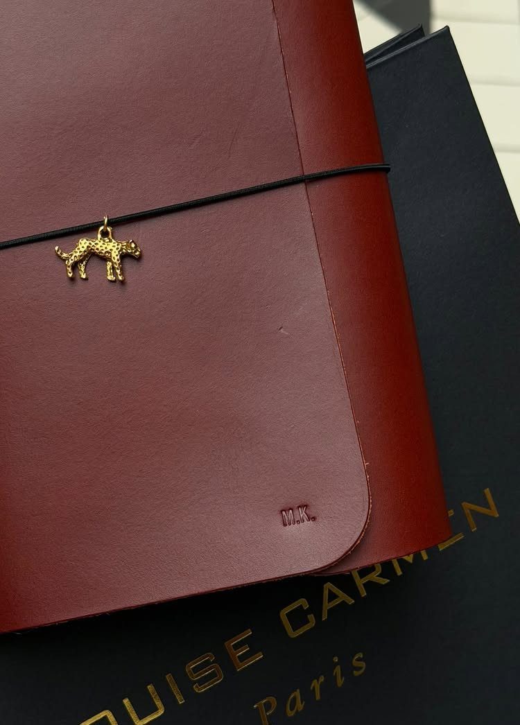 Reddish-brown leather journal with embossed initials and a gold camel charm.