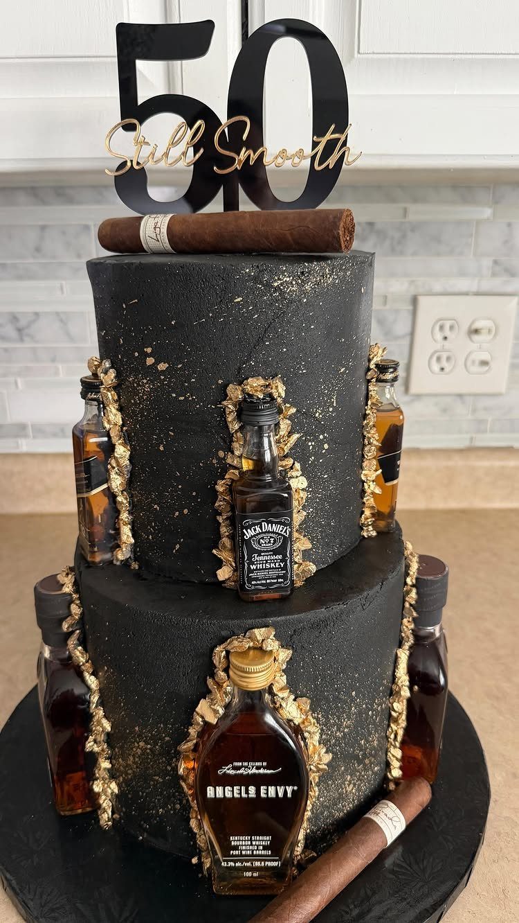 Two-tier black birthday cake with gold accents, mini whiskey bottles, cigars, and 50 topper.