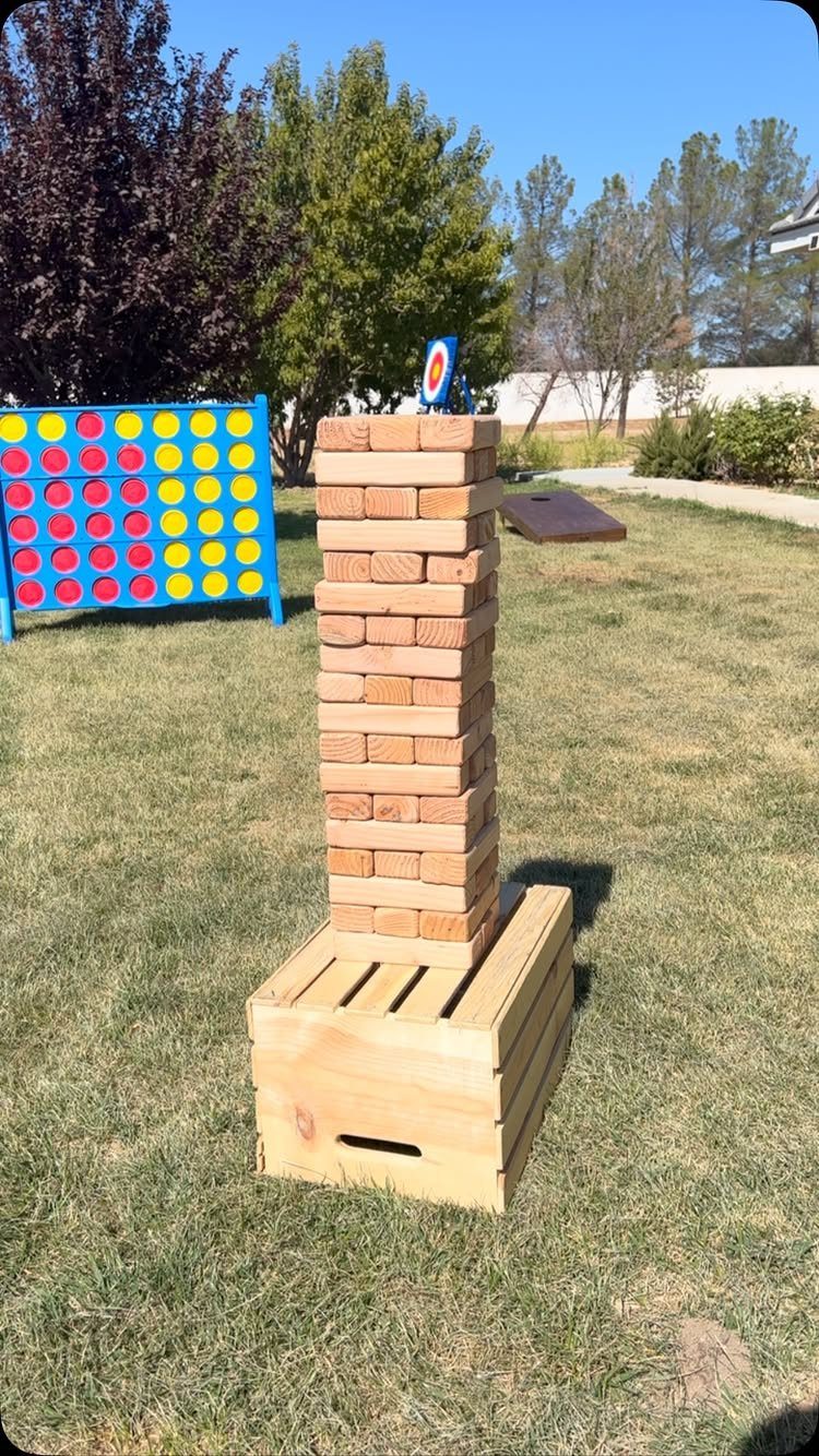 Giant wooden block tower and oversized Connect Four game on a grassy lawn.