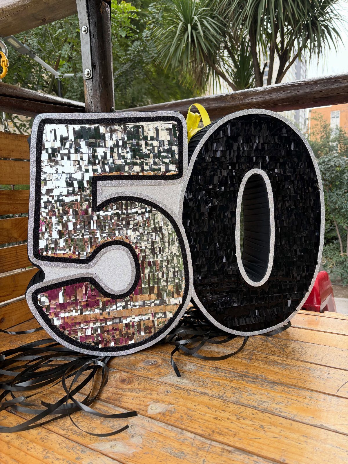 Number 50 piñata with silver mirrors and black fringe on a wooden deck