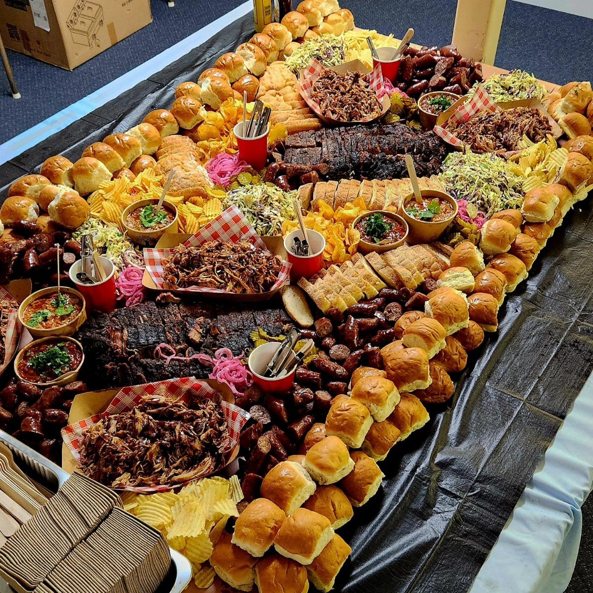 BBQ feast with ribs, pulled pork, sliders, and sides on a large table.