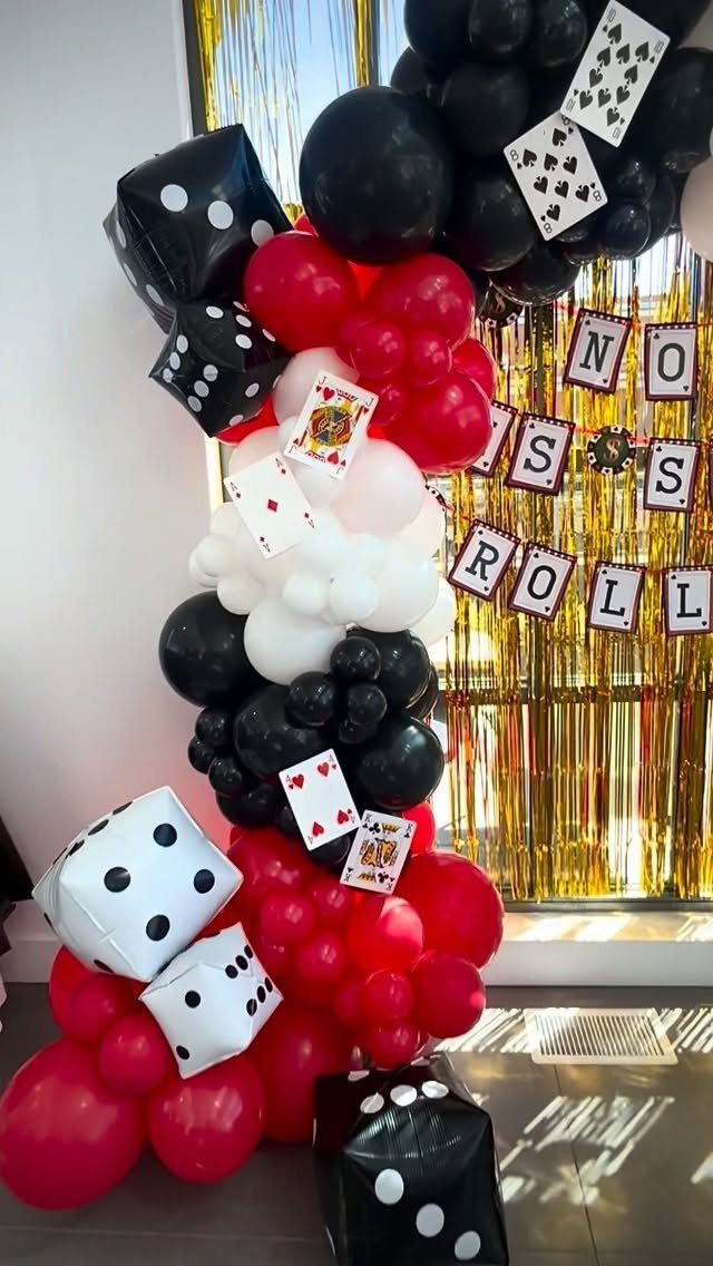 Balloon arch with red, black, and white balloons, dice, and playing cards.