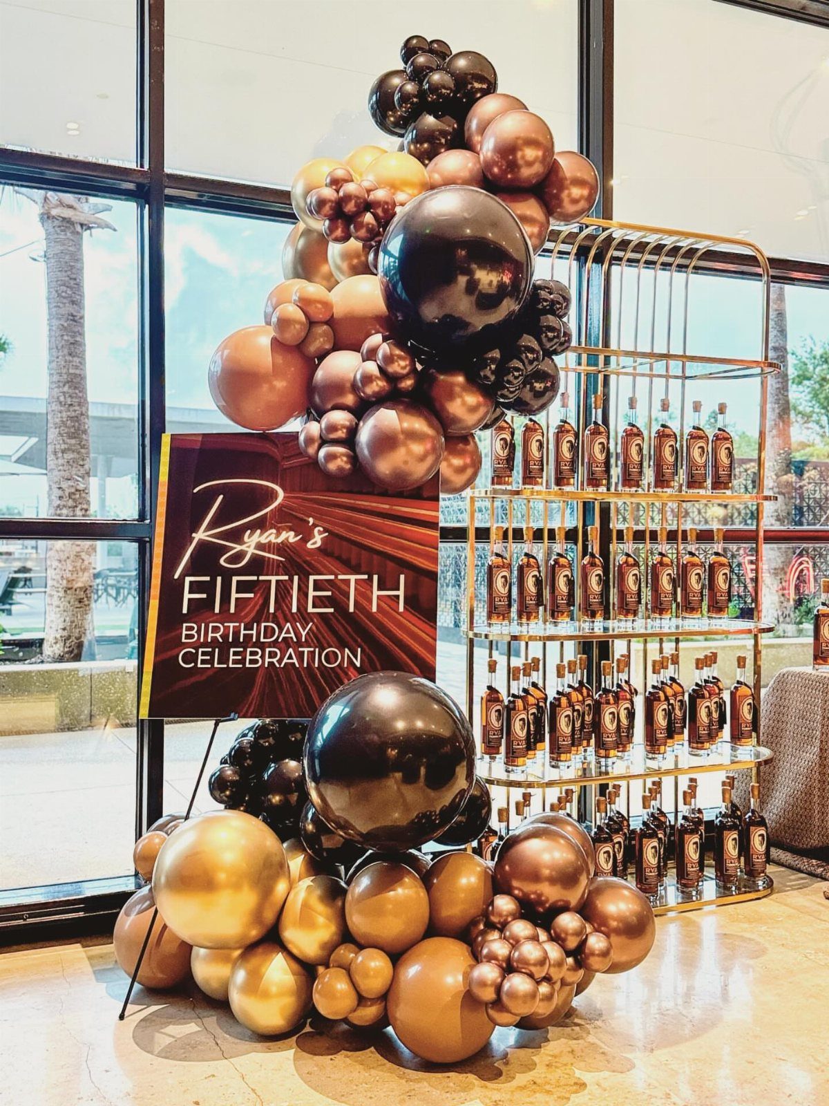Gold and black balloon arch next to a whiskey bottle display for a 50th birthday.