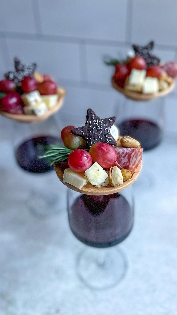 Red wine glasses topped with wooden platters of cheese, grapes, and nuts.