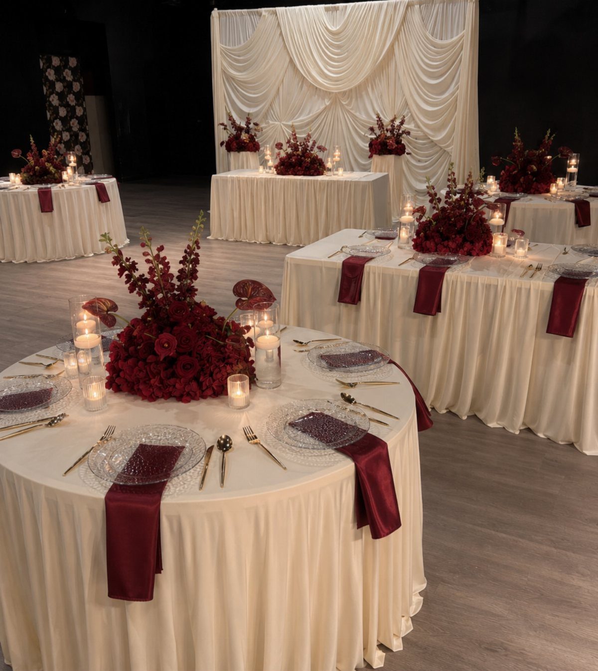 Cream banquet tables with burgundy napkins and red floral centerpieces in a hall.