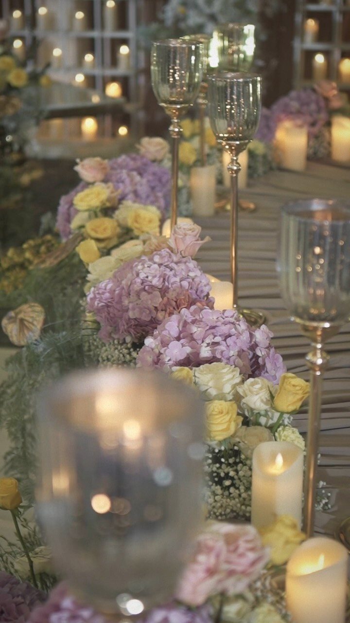 Floral arrangements of purple and yellow flowers with candles on a decorated table.