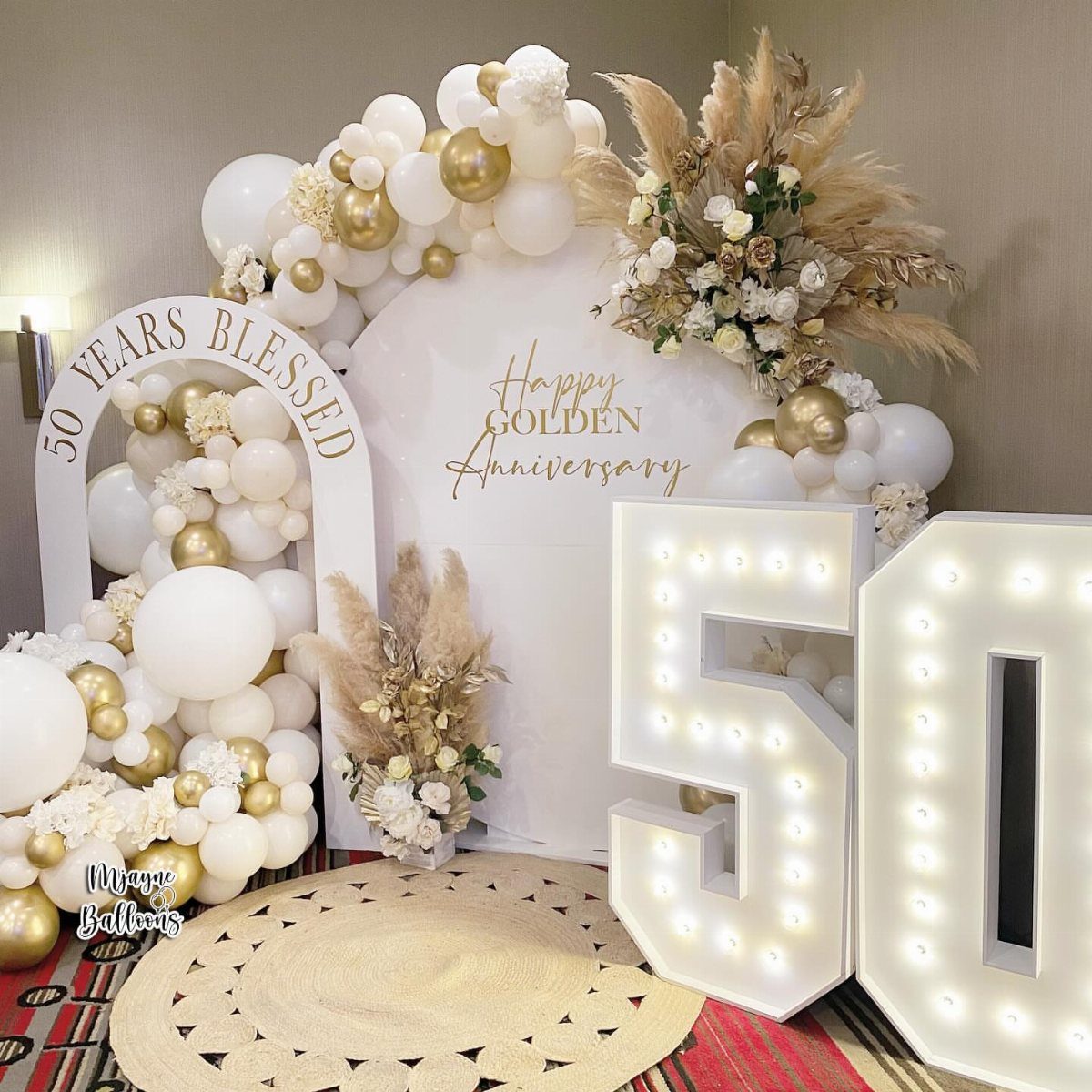 Golden anniversary decorations with white and gold balloons and large illuminated 50 numbers.