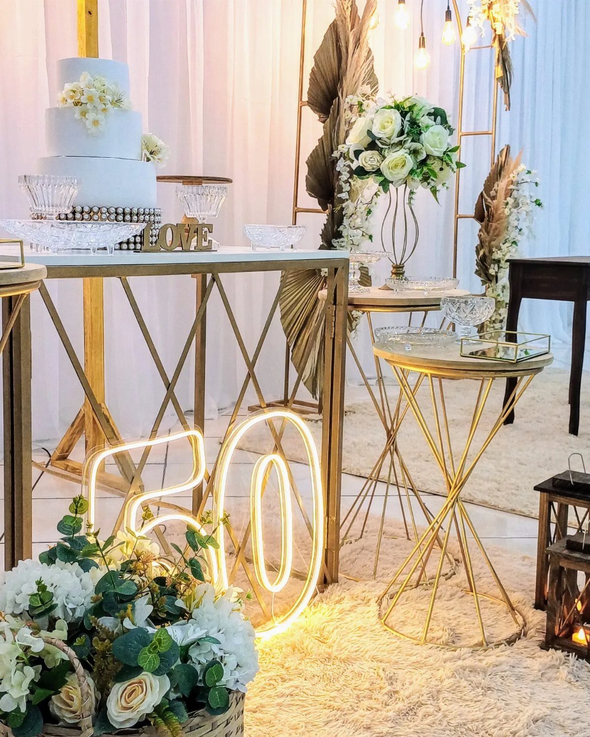 Celebratory 50th anniversary setup with white cake, neon 50 sign, and white flowers.