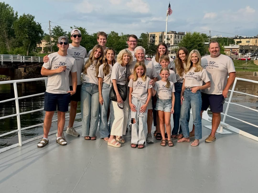 Multi-generational family in matching 50th anniversary shirts posing on a boat deck.