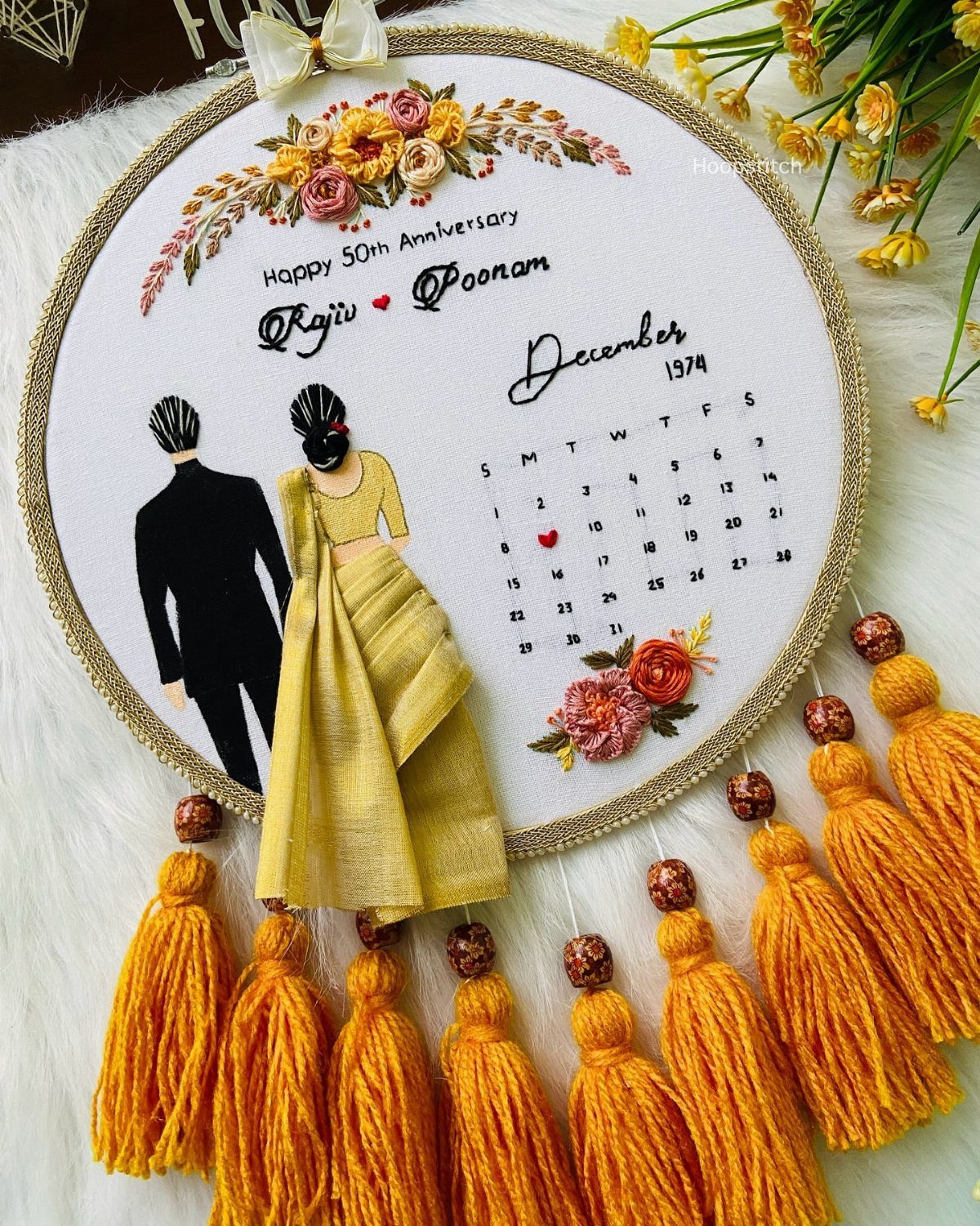 Custom anniversary embroidery hoop with a couple's illustration, calendar, and yellow tassels.