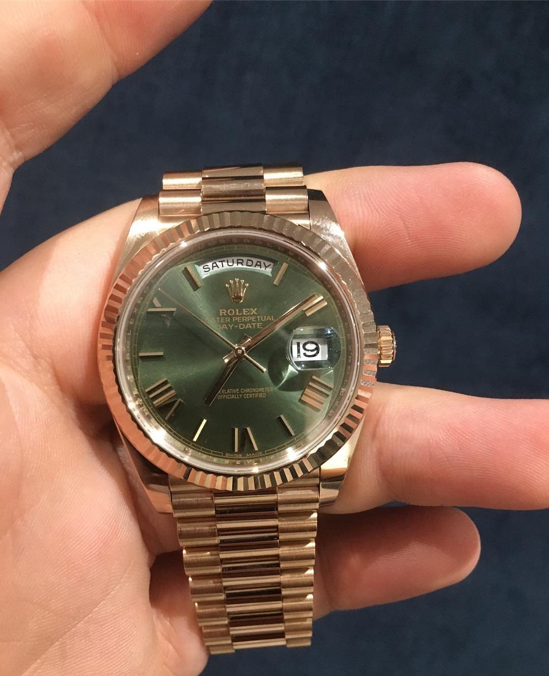 Gold Rolex watch with a green dial held in a person's hand.