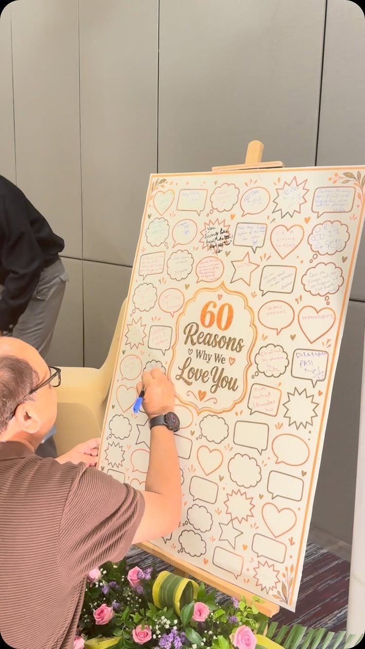 Man writing on a 60th birthday poster titled 60 Reasons Why We Love You