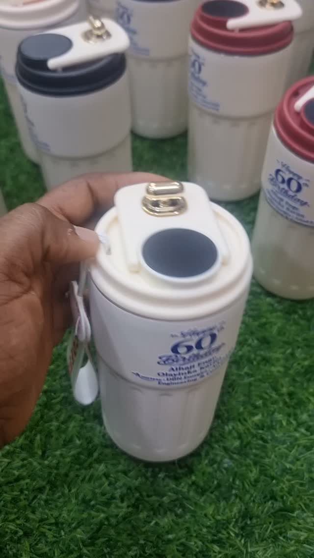 White insulated travel mug with 60th Birthday text held over green grass