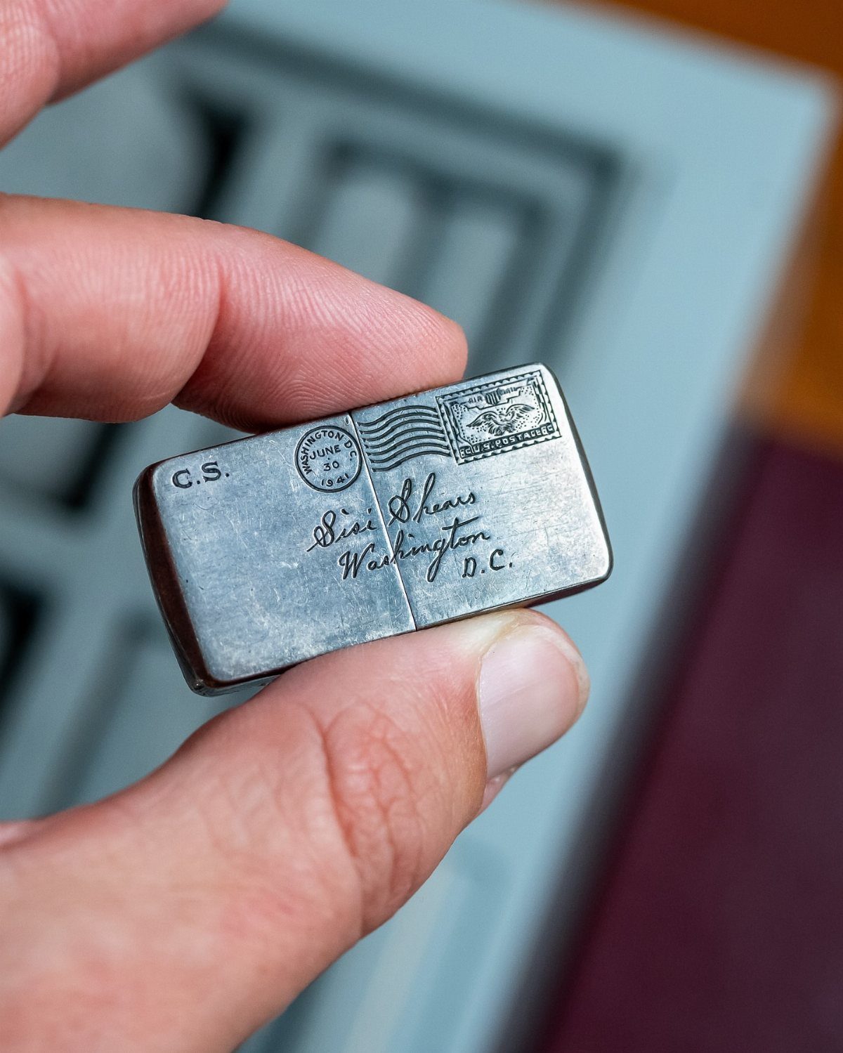 Small silver metal case with engraved vintage postage details held by fingers