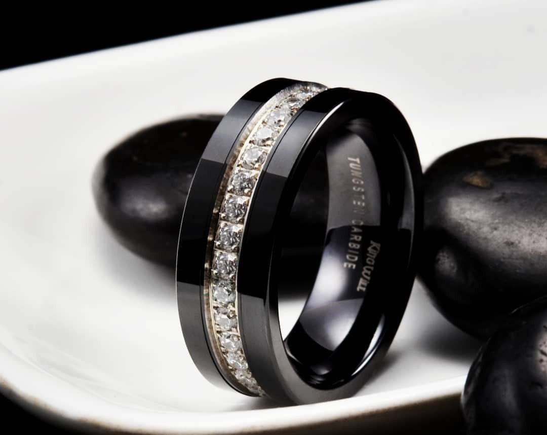 Black tungsten carbide ring with diamond inlay resting on white plate with black stones