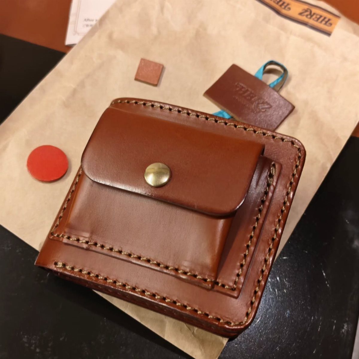 Brown leather wallet with a snap button on brown packing paper.