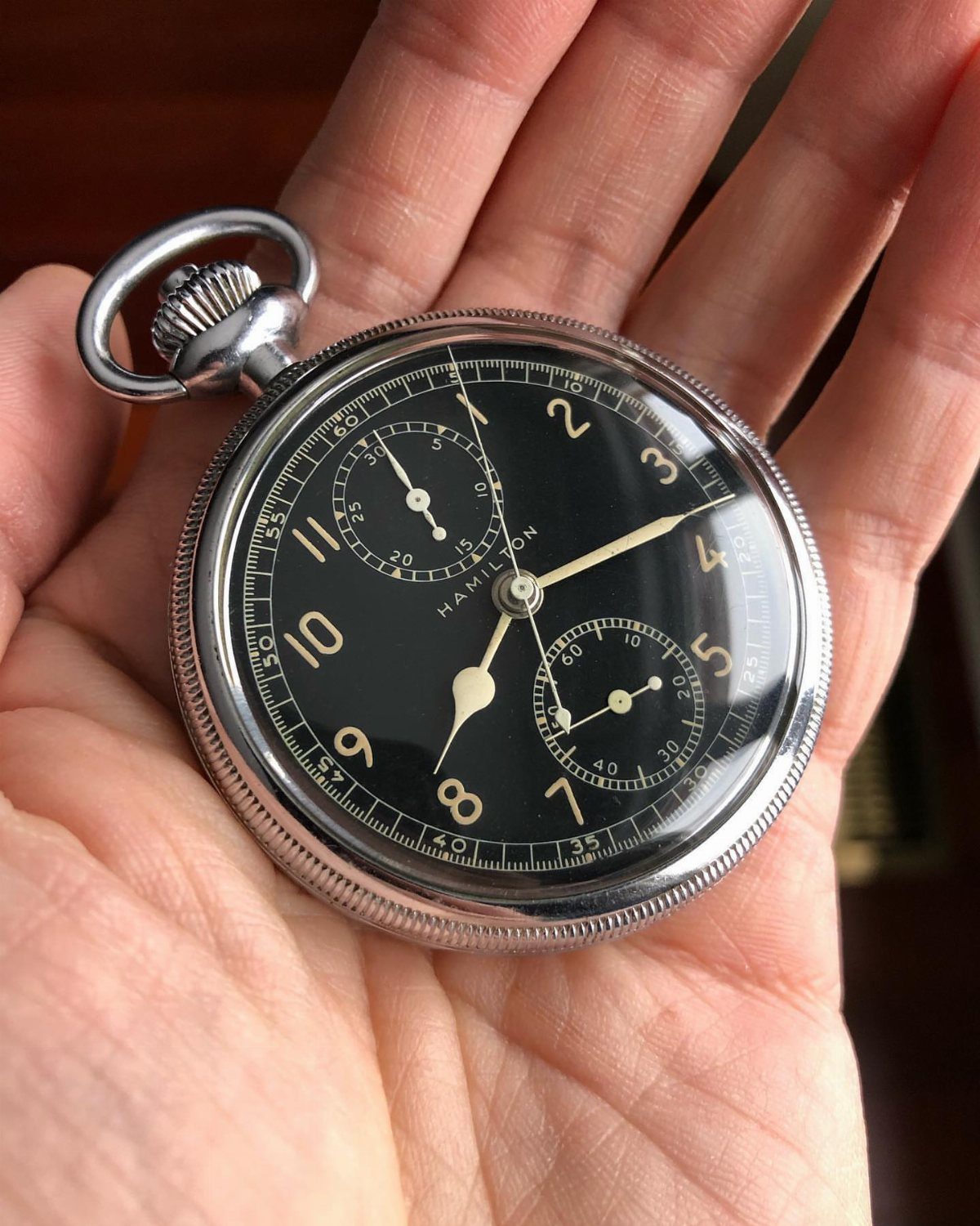 Silver Hamilton pocket watch with black face held in a person's open palm