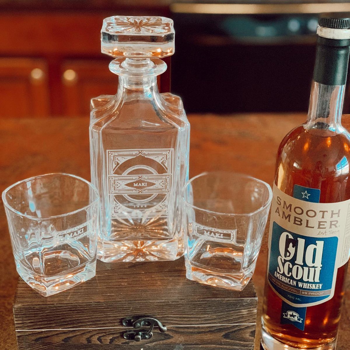 Whiskey decanter and matching glasses on a wooden box next to whiskey bottle