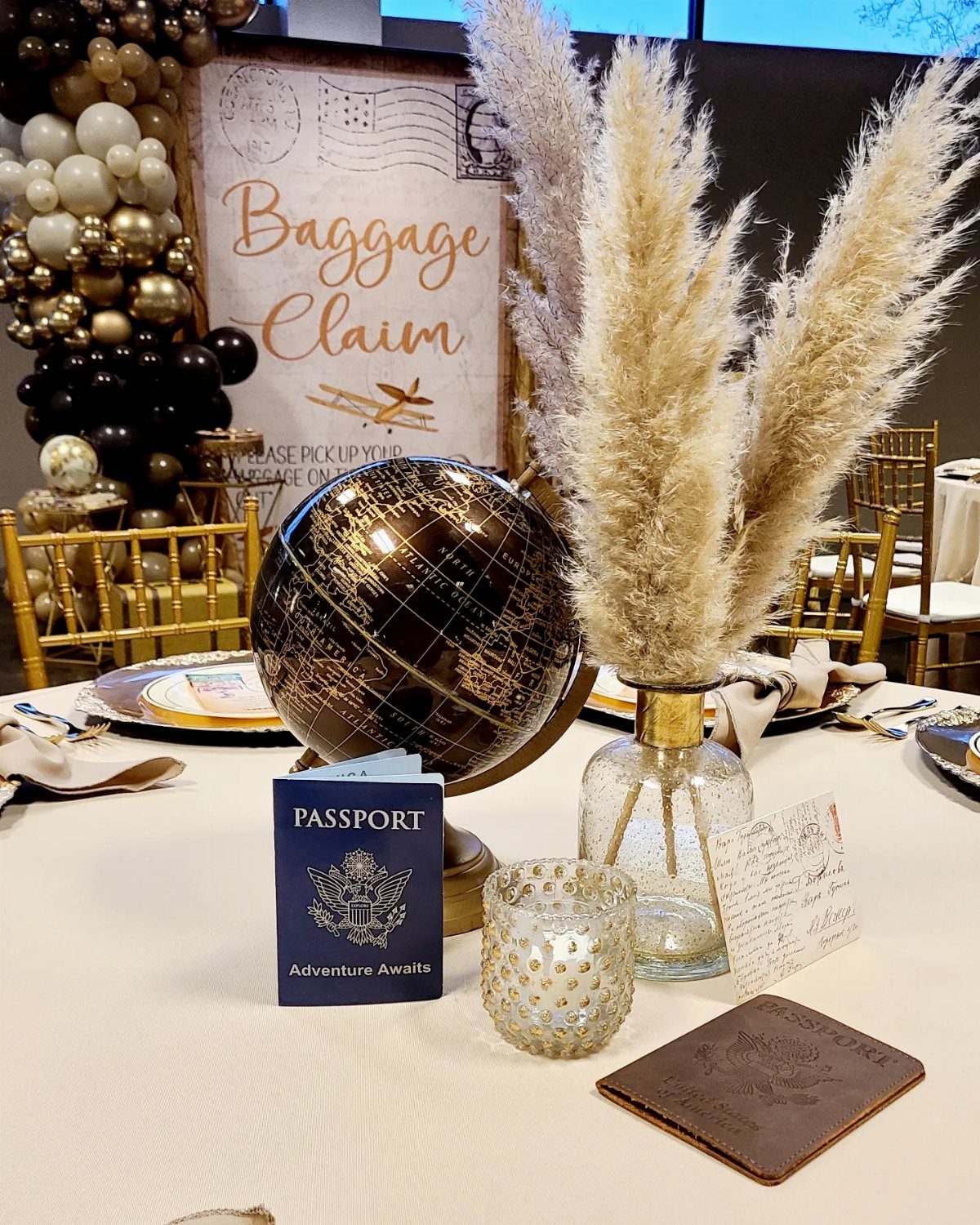 Travel-themed party table with a gold globe, passport prop, and pampas grass.