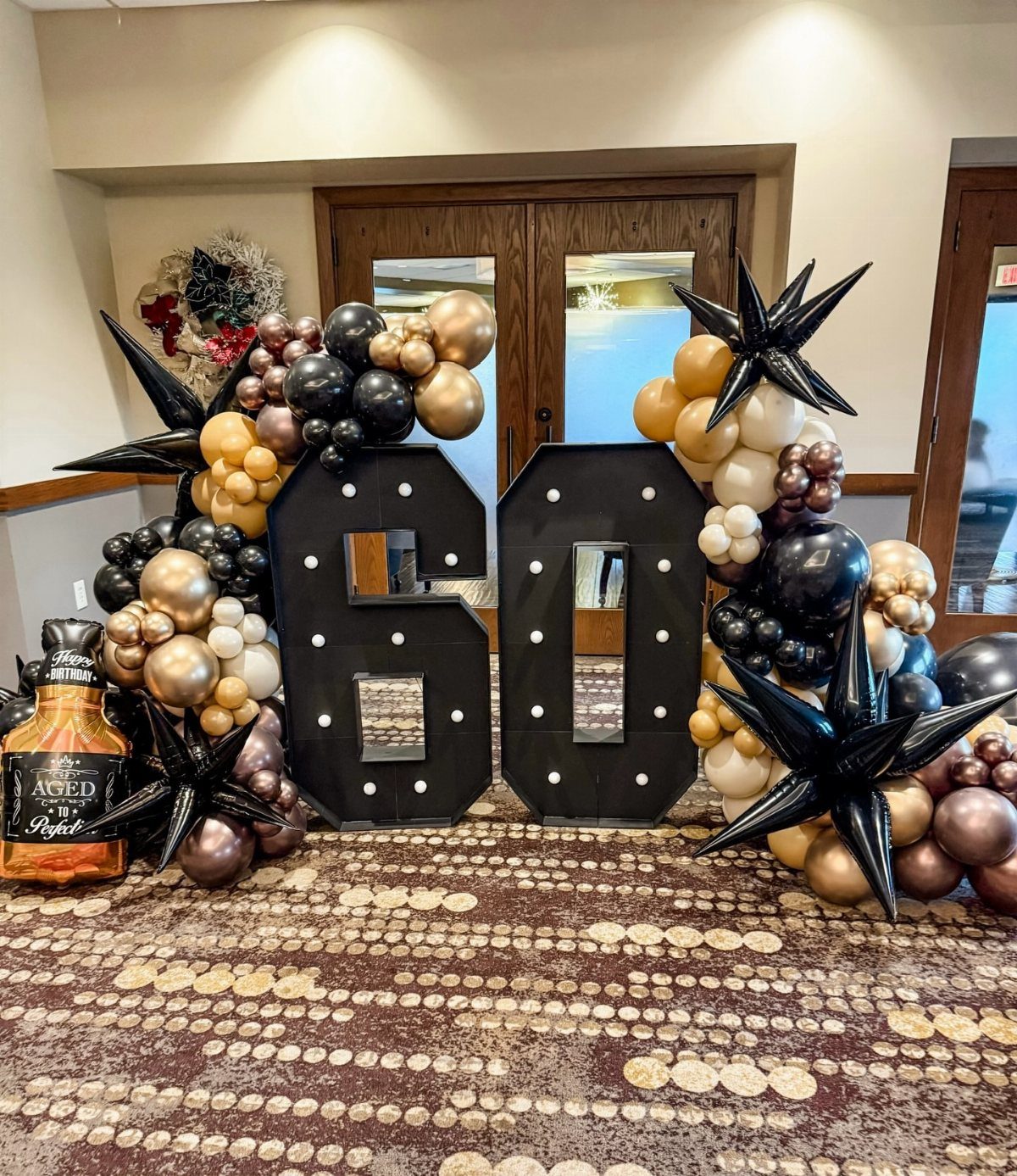Large black number 60 decorations surrounded by gold and black balloons and whiskey.