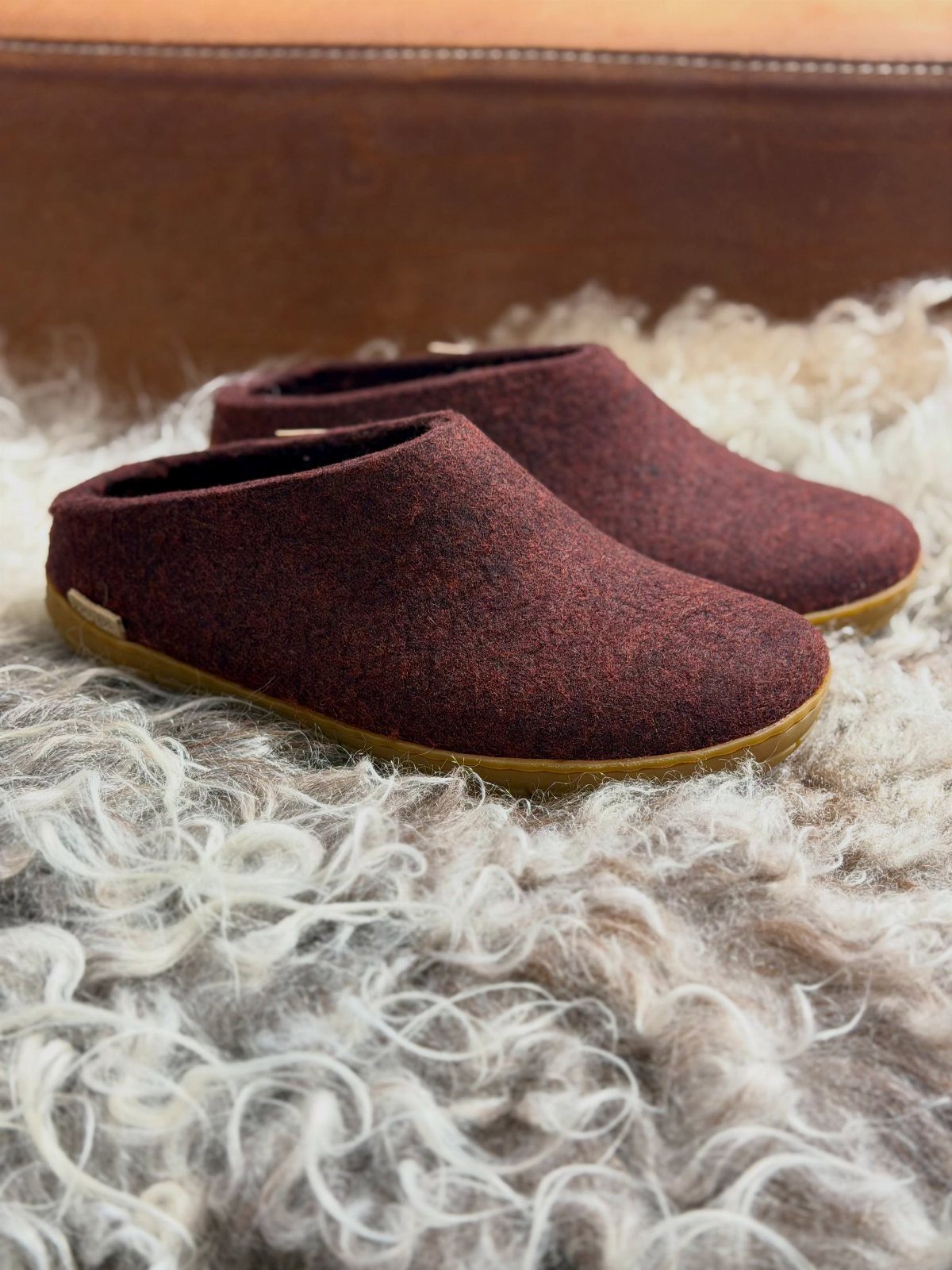 Dark red felted wool slippers resting on a fluffy white faux-fur rug.