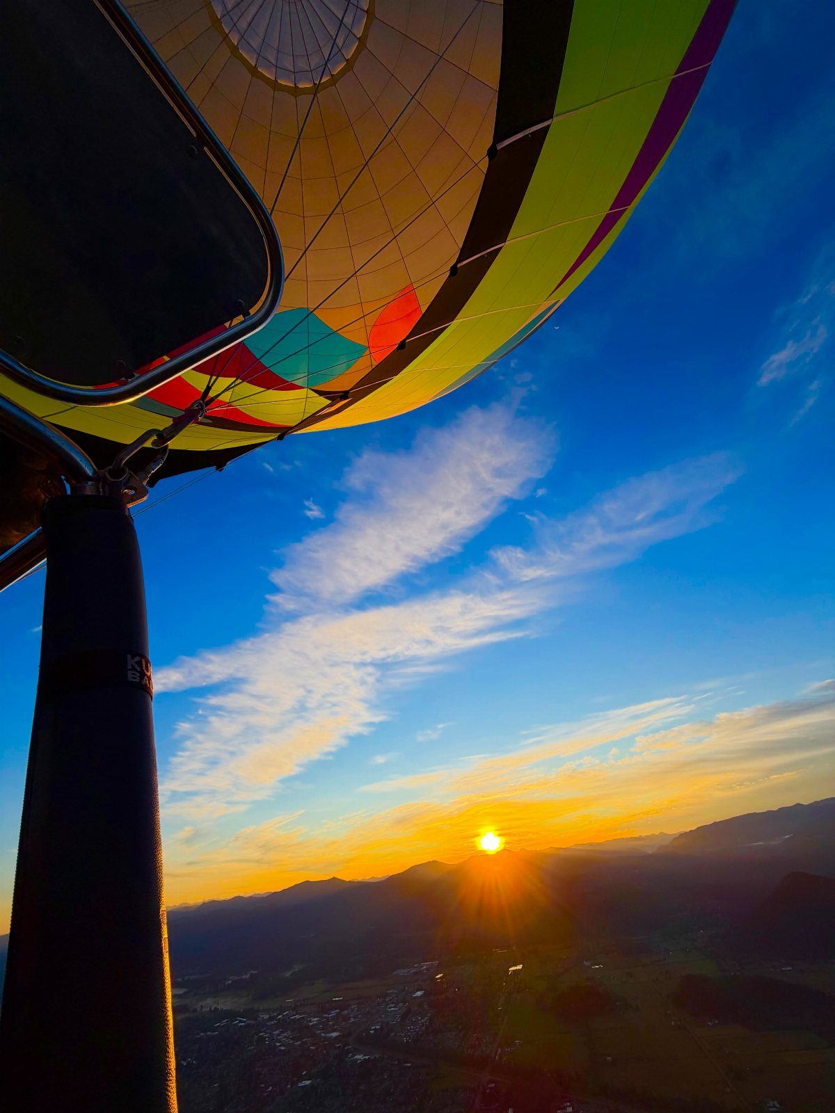 Hot air balloon floating over mountains during a vibrant golden sunrise.
