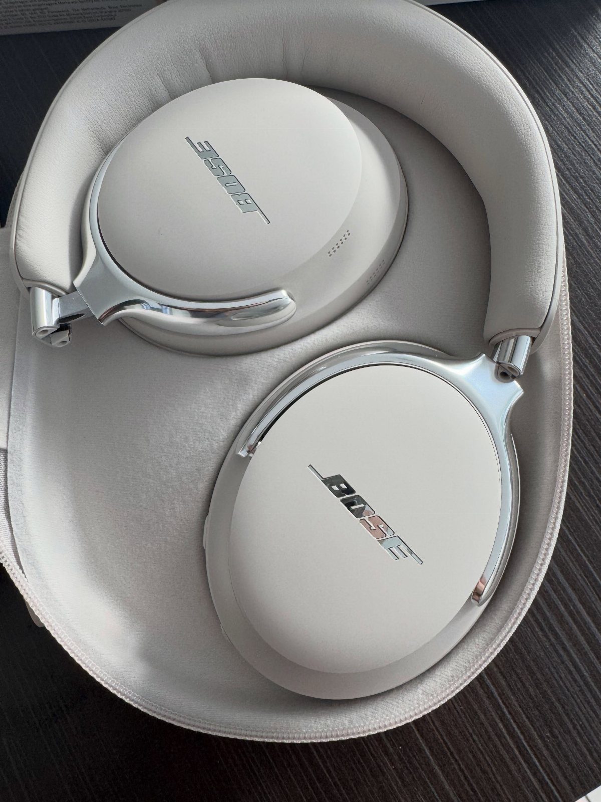 White Bose headphones resting inside a white protective carrying case on dark wood.