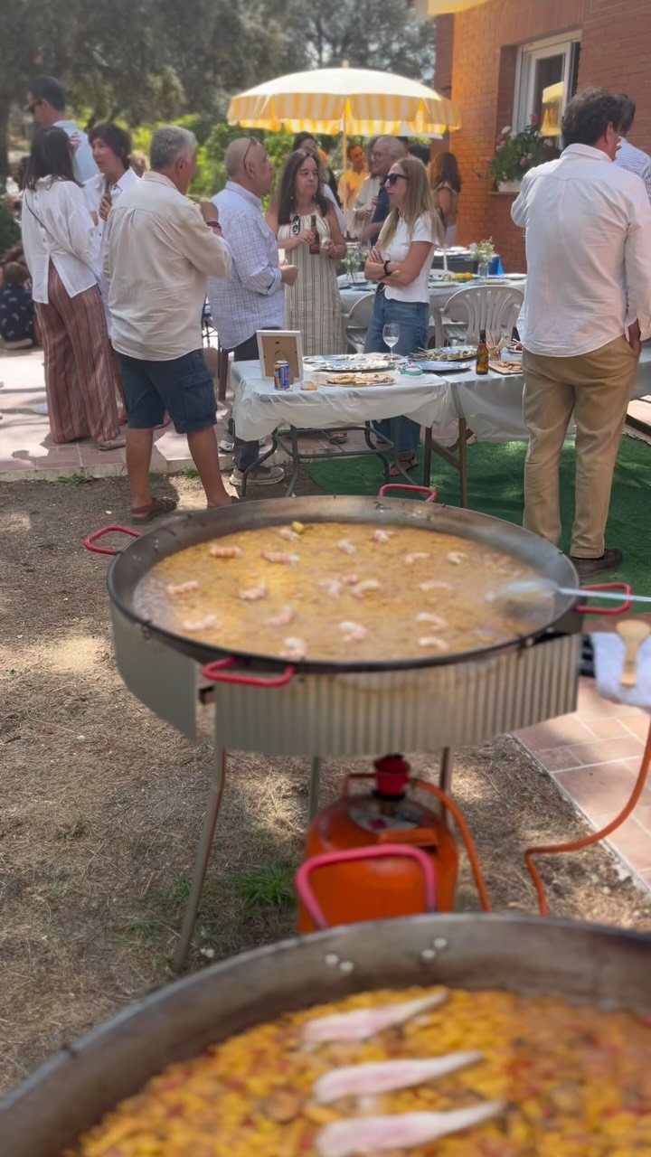 Large pans of paella at an outdoor garden party with guests socializing.
