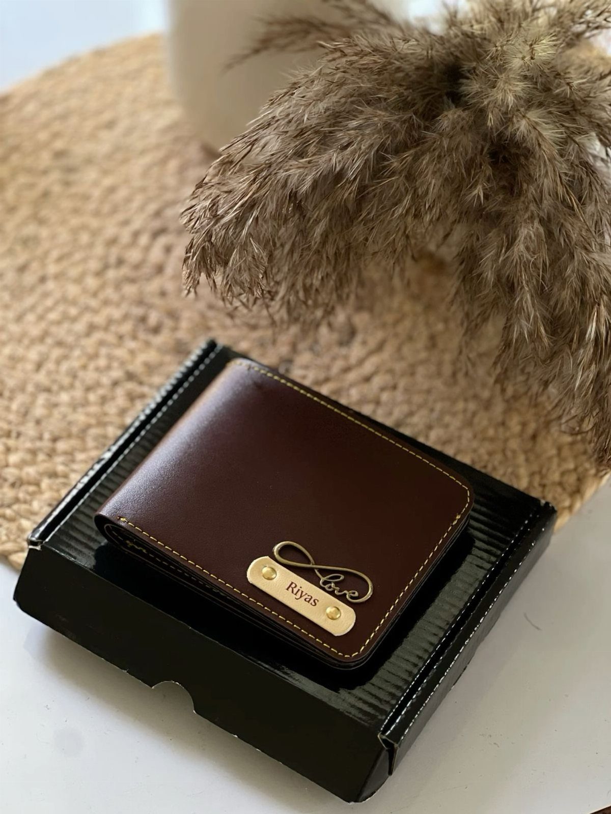 Brown leather wallet with personalized gold nameplate resting on a black gift box.