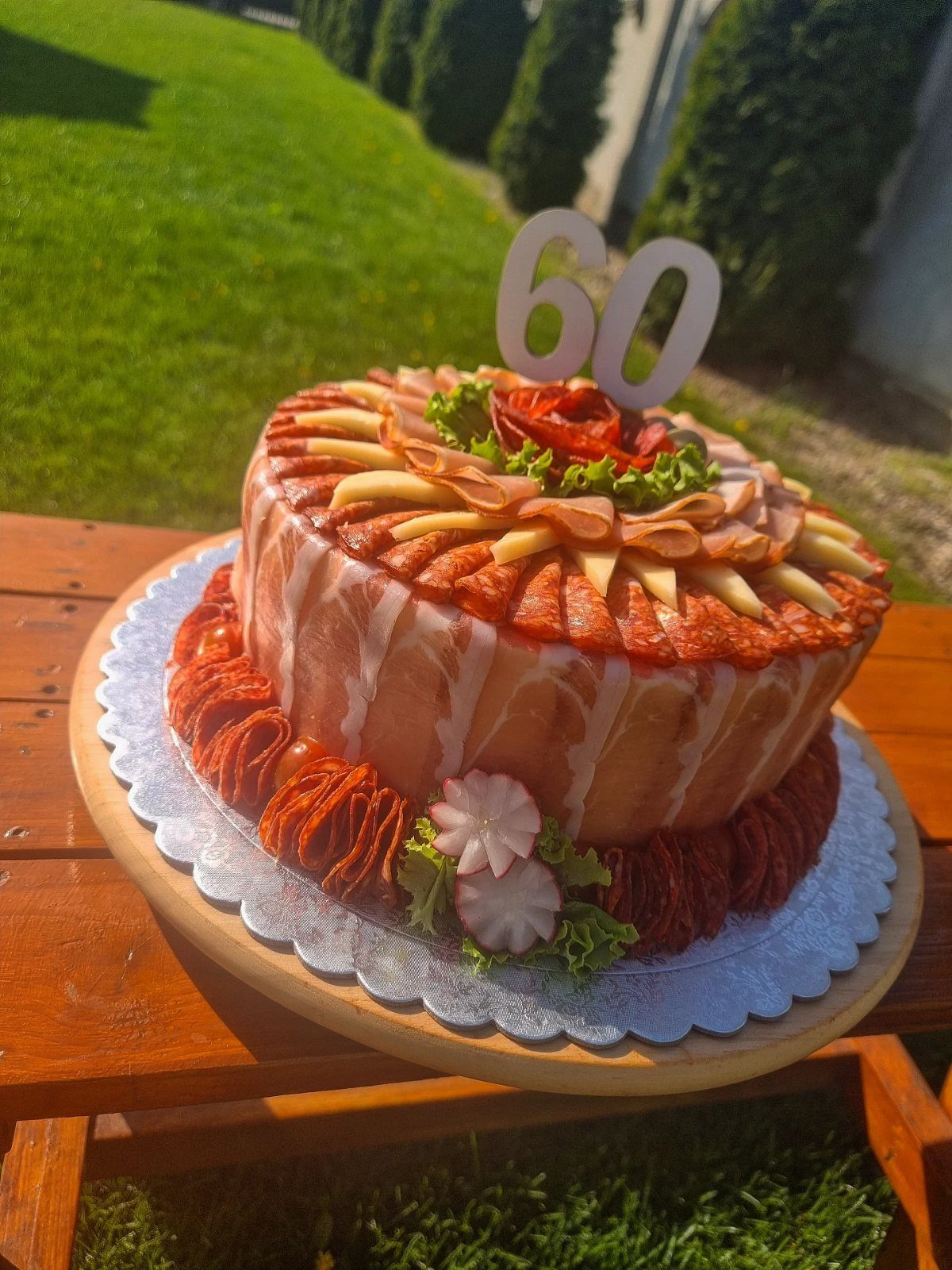 Savory meat cake decorated with cheese and a number 60 topper outdoors.