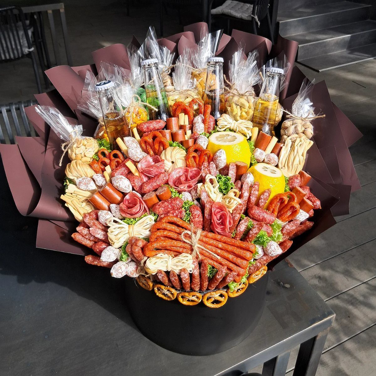 Edible meat bouquet with sausages, pretzels, and small bottles in a black pot.