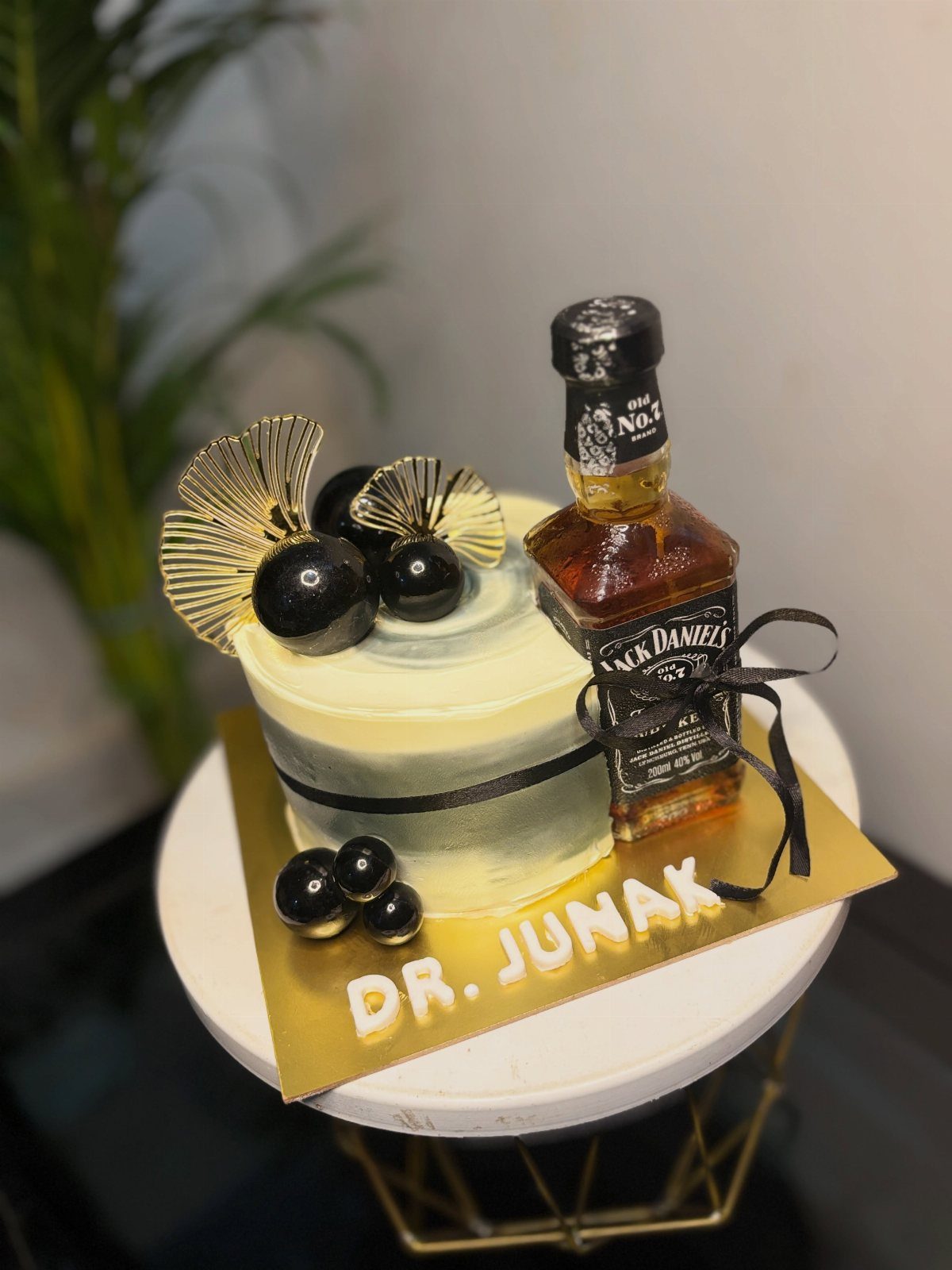 White frosted cake topped with a Jack Daniel's bottle and gold decorations.