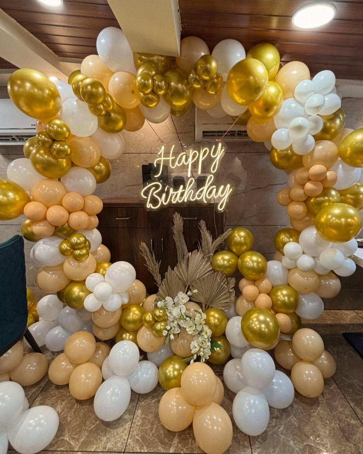 Gold, white, and peach balloon arch with a glowing Happy Birthday neon sign.