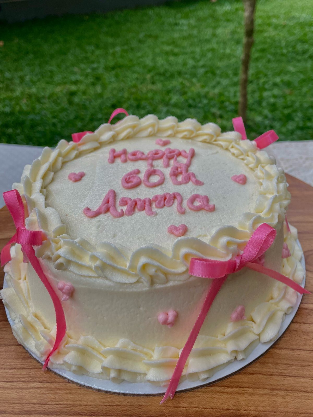 White frosted birthday cake with pink ribbons and Happy 60th Amma icing