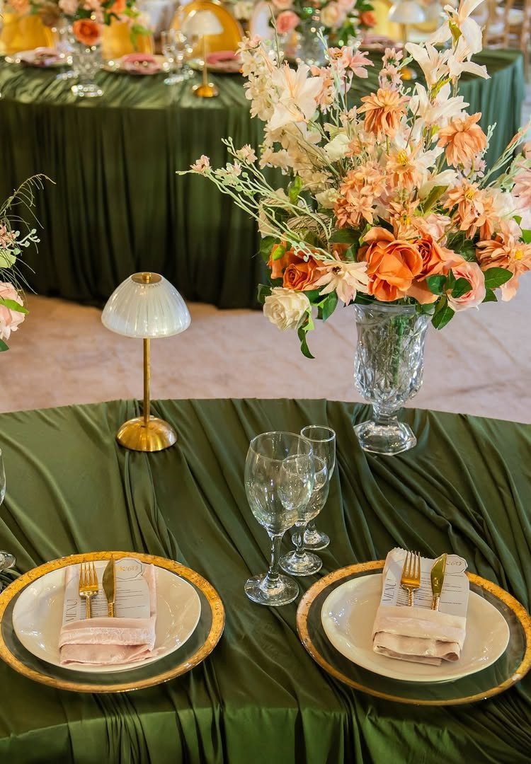 Elegant table setting with green satin cloth, peach floral centerpiece, and gold accents.