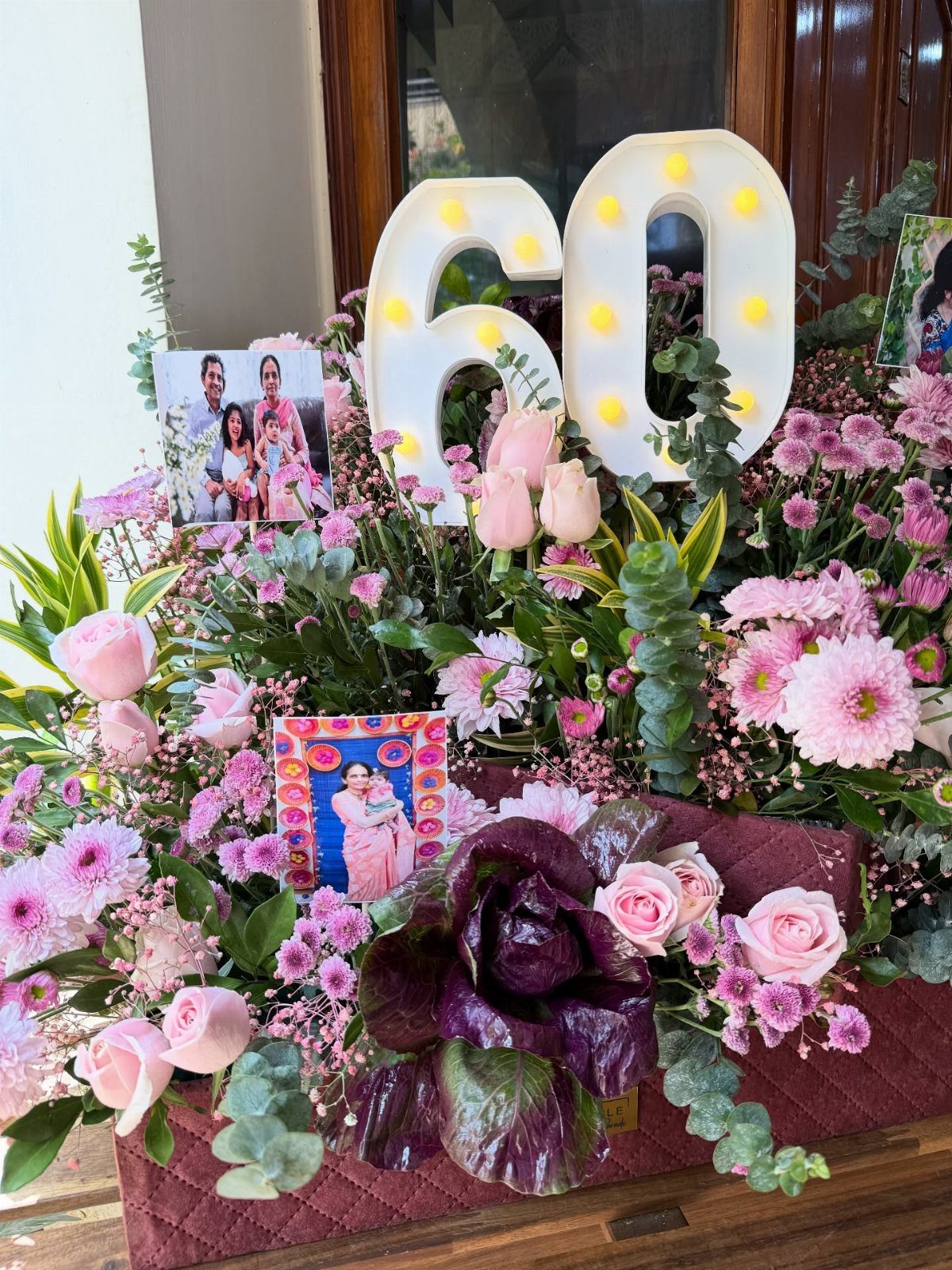 Floral arrangement with illuminated number 60 and family photos for a birthday celebration