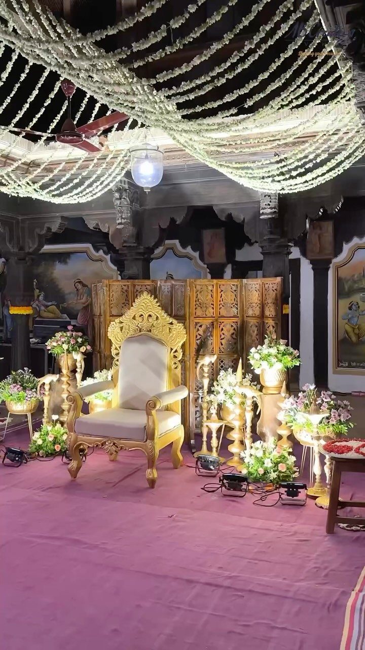 Ornate gold throne chair surrounded by white floral arrangements and hanging flower garlands.