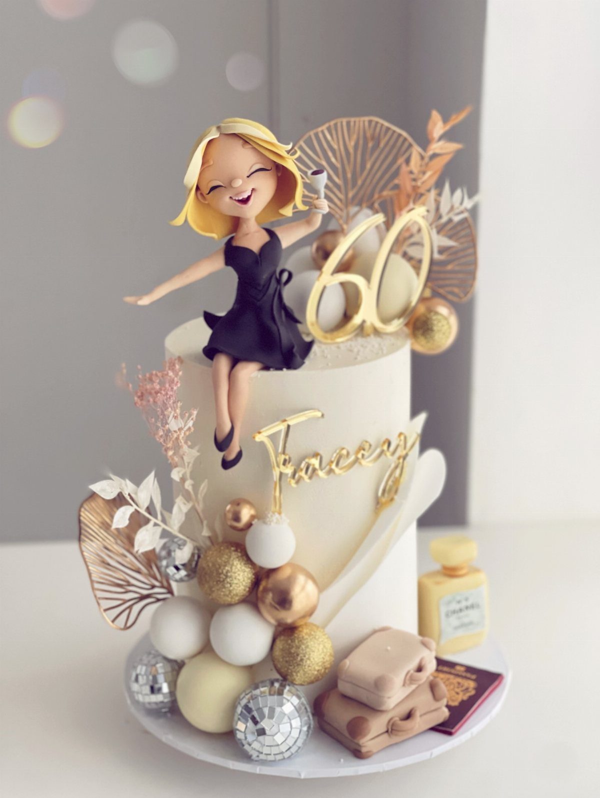 White birthday cake with a woman figure, gold 60 topper, and travel accessories.