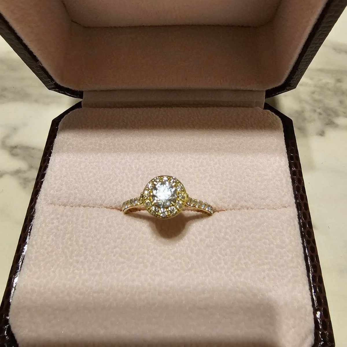 Gold diamond ring in a brown velvet jewelry box on marble surface