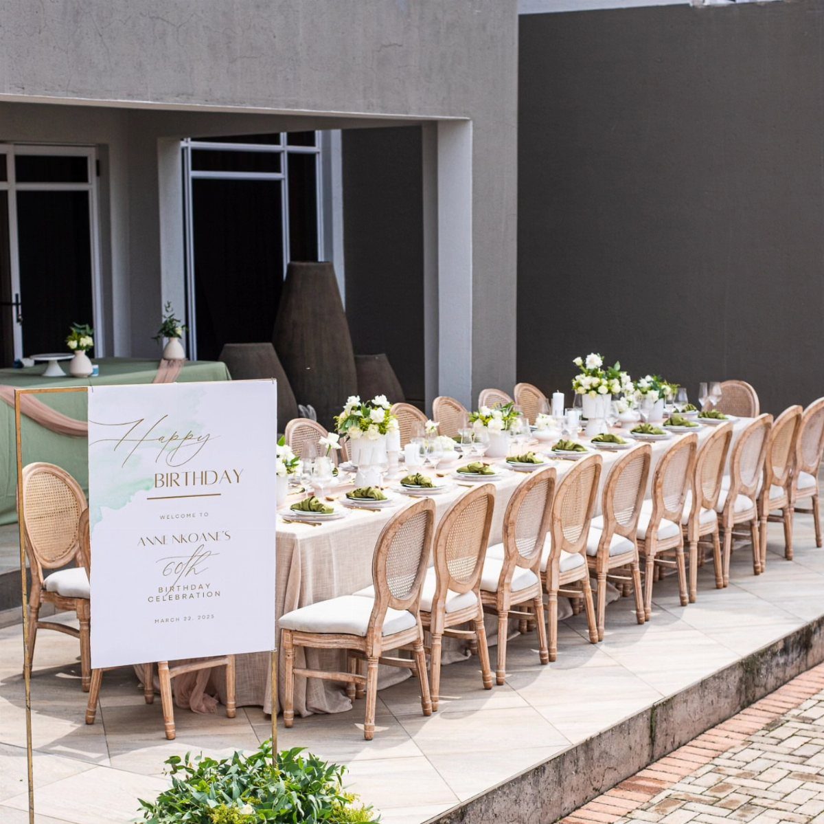 Outdoor dining table with white flowers and wicker chairs for a 60th birthday party.