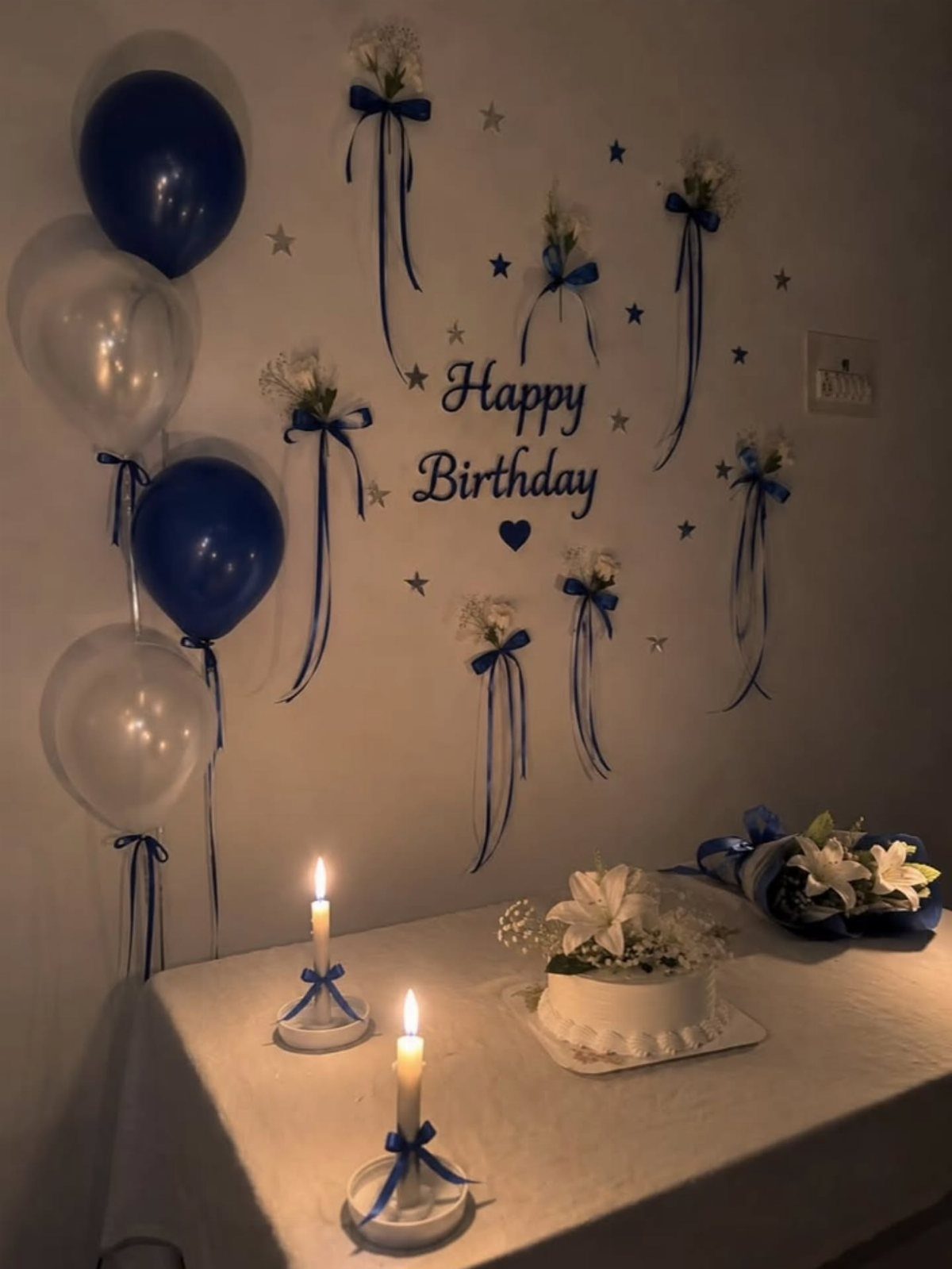 Birthday party setup with blue balloons, a white cake, and lit candles.