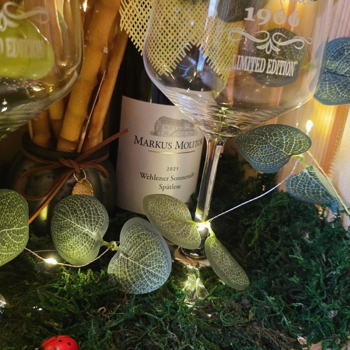 Etched wine glass and bottle of wine on moss with fairy lights