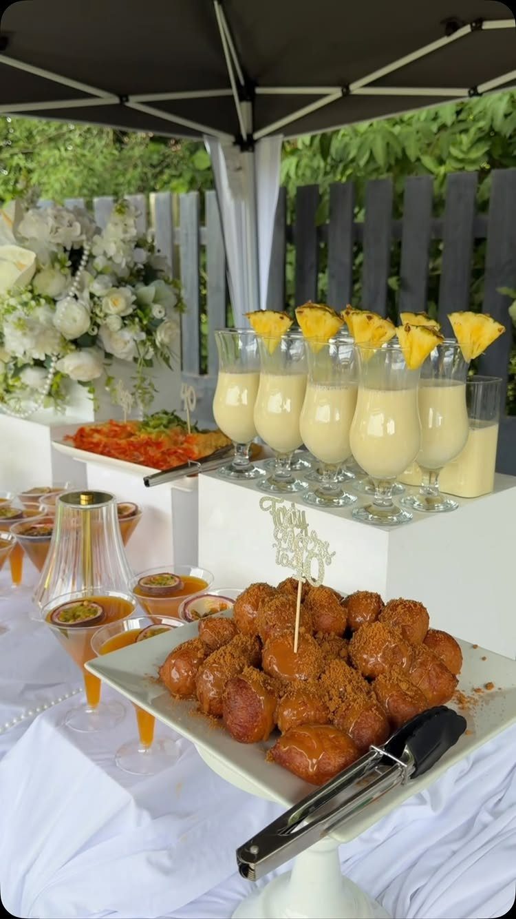 Catering spread with cinnamon donut holes and pineapple cocktails under a black umbrella.