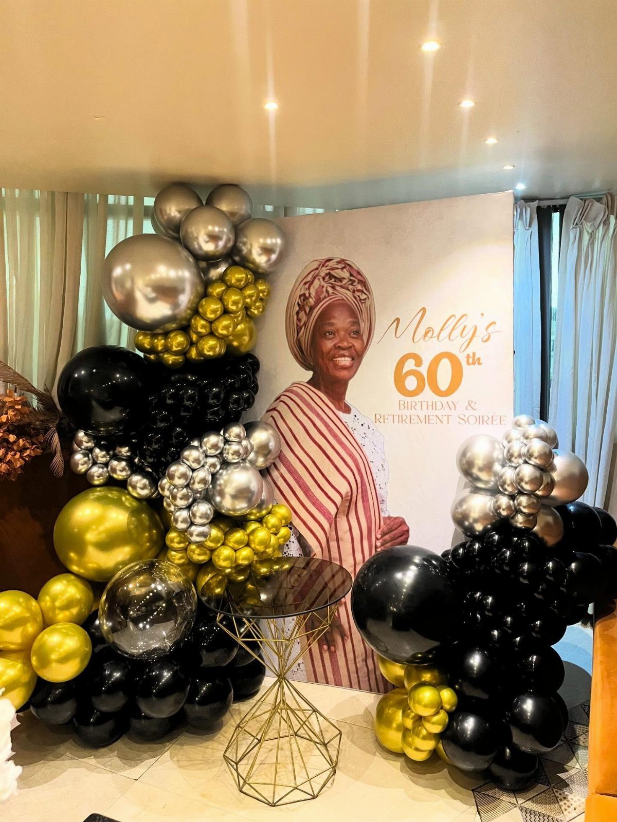 Birthday banner of a woman with gold, silver, and black balloon decorations.