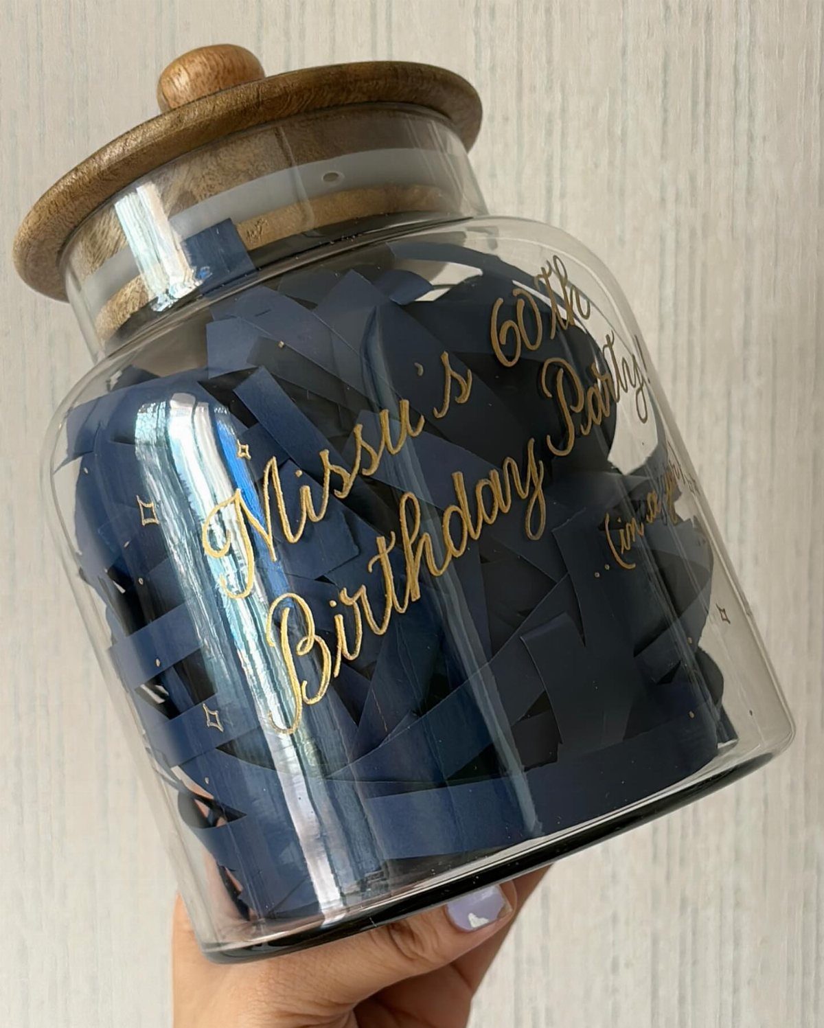 Glass jar with wooden lid filled with blue paper notes for 60th birthday