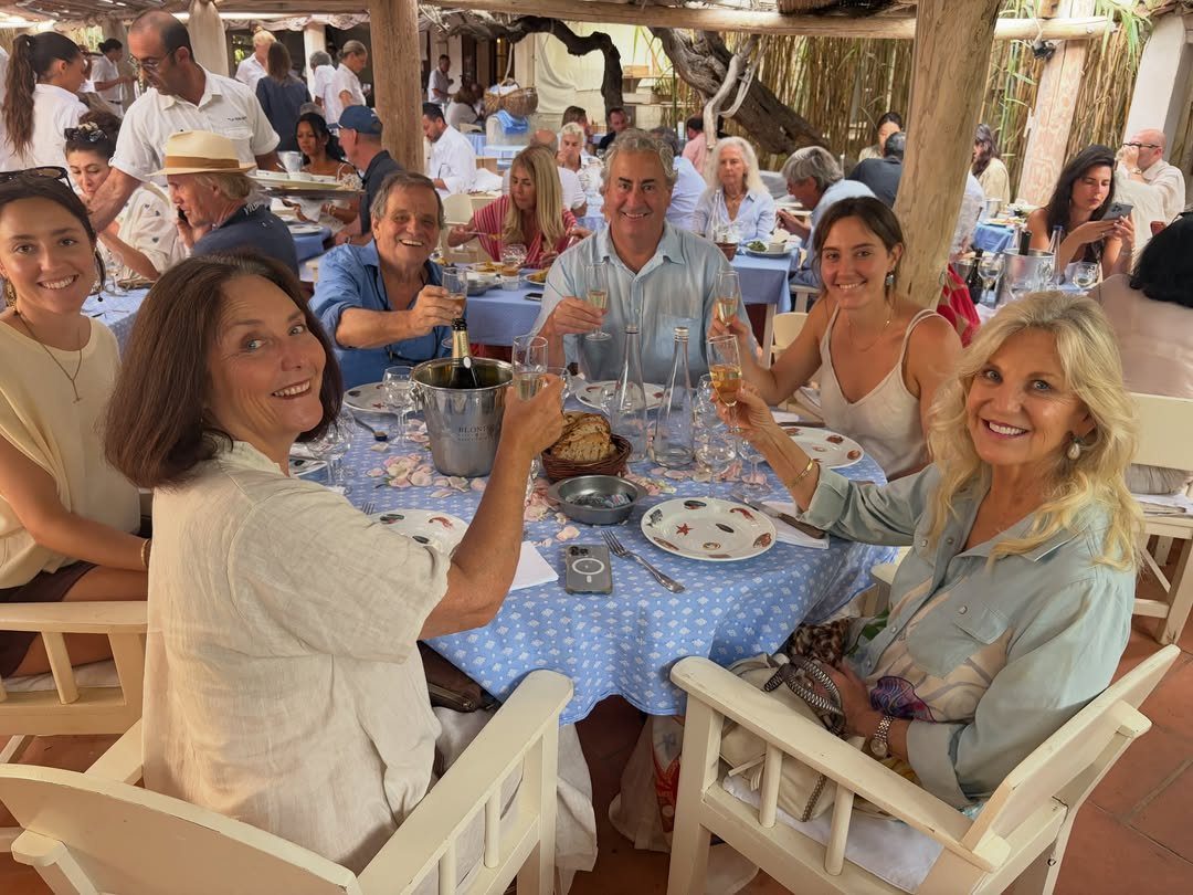 Group of adults toasting with champagne glasses at an outdoor garden lunch table.