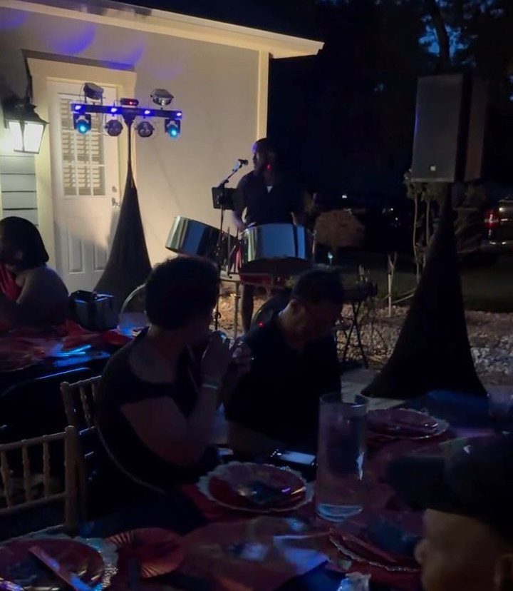 People dining outdoors at night with a steel drum musician performing nearby.